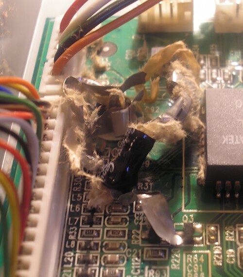 Un condensateur électrolytique explosé, montrant des fragments de papier et de feuille métallique