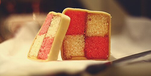 Gâteau Battenberg fait maison recouvert de pâte d'amande et, lorsqu'il est coupé en coupe transversale, présentant un motif à carreaux distinctif deux par deux alternativement coloré en rose et en jaune