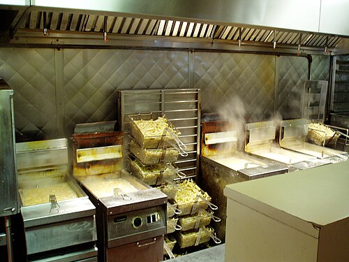 Une rangée de cinq friteuses, toutes fumantes et remplies de paniers de frites.