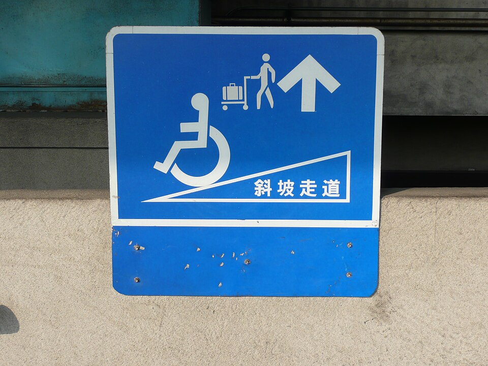Un panneau bleu à bordure blanche et portant un texte affiche le dessin d'une personne en fauteuil roulant.